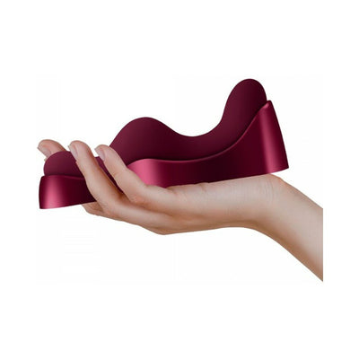Hand holding a compact, curved Ruby Glow Rosa Saddle Vibrator in deep burgundy color.