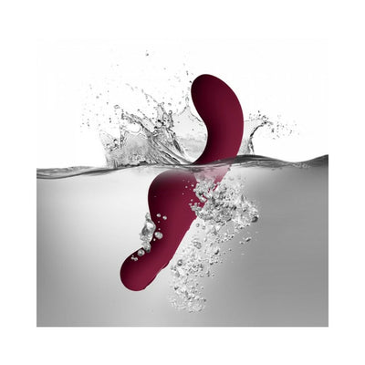 Ruby Glow Rosa Saddle Vibrator in deep red shown submerged in water with bubbles, highlighting its waterproof design.