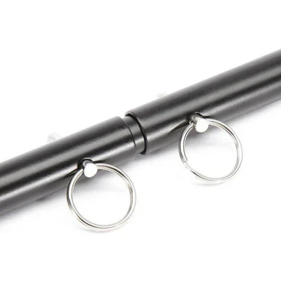 Close-up of black adjustable spreader bar with metal attachment rings on a white background.