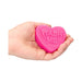Hand holding a bright pink heart-shaped soap bar embossed with the words "WASH ME" on a white background.