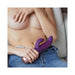 Person holding a purple dual-stimulation vibrator with textured design while reclining in jeans.