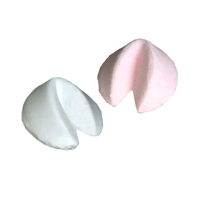 Two pastel-colored fortune cookie shaped bath bombs, one white and one light pink, on a white background.