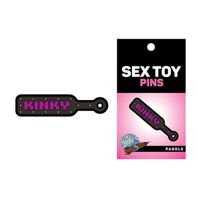 Black enamel pin shaped like a paddle with purple "KINKY" text and silver studs, displayed with packaging card.
