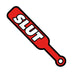 Red enamel lapel pin shaped like a BDSM paddle with bold white text reading "SLUT" and a small handle hole.