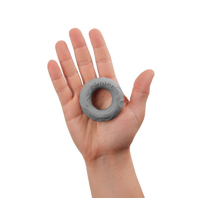 Hand holding a small gray silicone Shaft C-ring with textured surface and embossed logo.