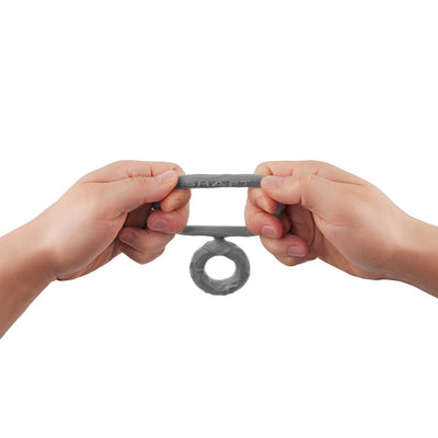 Hands stretching a flexible gray double C-ring made of soft silicone with the brand name Shaft embossed on it.