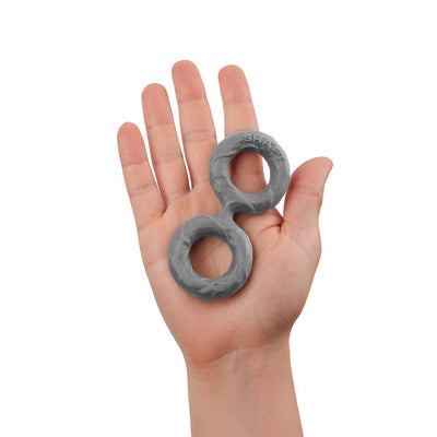 Hand holding a medium-sized gray double C-ring made of flexible silicone with textured surface and "SHAFT" branding.