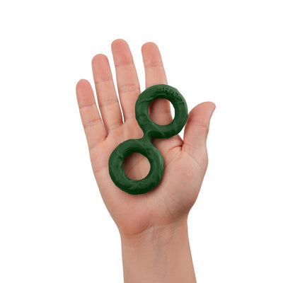 Hand holding a medium-sized dark green double C-ring made of flexible silicone material.