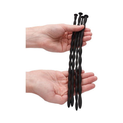 Hands holding four black silicone spiral urethral sounding plugs of varying thicknesses.