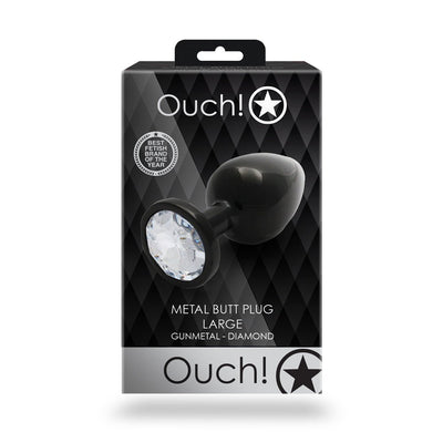 Packaging of Shots Ouch! large gunmetal metal butt plug with a clear gem base on a black diamond-patterned background.