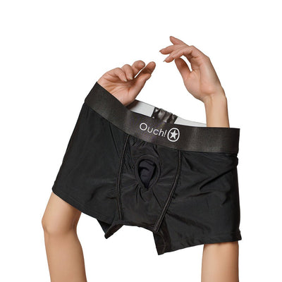 Hands holding black mid-rise vibrating strap-on brief with Ouch! branded waistband and central O-ring opening.