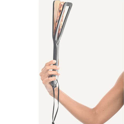 Hand holding a tortoiseshell-inspired spanker paddle with black handle and attached wrist strap against a plain background.