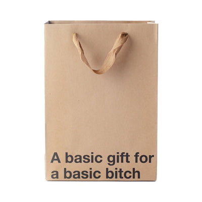 Kraft paper gift bag with brown ribbon handles and bold black text reading a basic gift for a basic bitch.