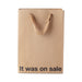 Brown kraft gift bag with brown ribbon handles and "It was on sale" printed in bold black text at the bottom.