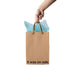 Hand holding a brown kraft gift bag with brown ribbon handles and blue tissue paper, printed with "It was on sale" text.