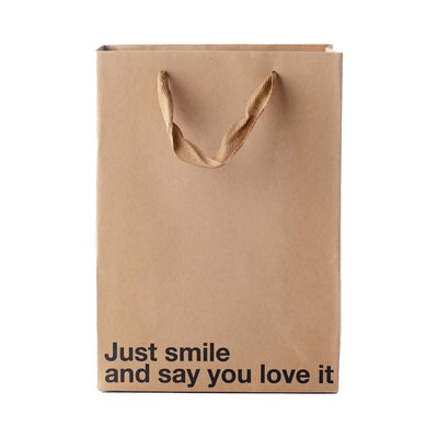 Kraft paper gift bag with brown ribbon handles and black text reading Just smile and say you love it.