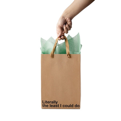 Hand holding a kraft gift bag with brown ribbon handles and green tissue paper, printed with "Literally the least I could do" text.