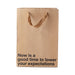 Brown kraft gift bag with brown ribbon handles and black text reading Now is a good time to lower your expectations