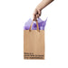Hand holding a kraft gift bag with brown ribbon handles and purple tissue paper, printed with "Now is a good time to lower your expectations" text.