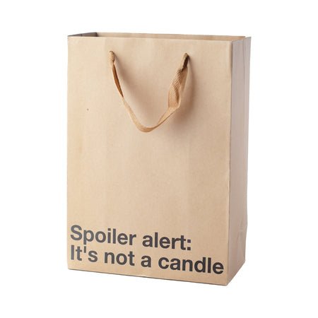 Kraft gift bag with brown ribbon handles and text "Spoiler alert: It's not a candle" in black lettering.