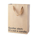Kraft gift bag with brown ribbon handles and text "Spoiler alert: It's not a candle" in black lettering.