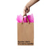 Hand holding a Kraft gift bag with brown ribbon handles and pink tissue, text reads Spoiler alert: It's not a candle.