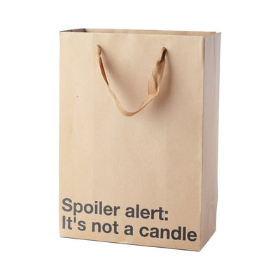 Kraft paper gift bag with brown ribbon handles and black text reading "Spoiler alert: It's not a candle"