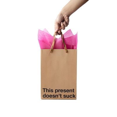 Hand holding a kraft gift bag with brown ribbon handles and pink tissue paper, featuring the phrase This present doesn't suck.