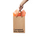 Hand holding a kraft gift bag with brown ribbon handles and orange tissue paper, printed with "I wrapped this myself" text.