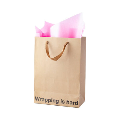 Kraft gift bag with brown ribbon handles and pink tissue paper, printed with "Wrapping is hard" text at the bottom.