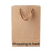 Kraft paper gift bag with brown ribbon handles and "Wrapping is hard" printed in black at the bottom front.