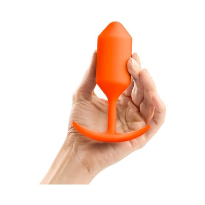 Hand holding bright orange seamless silicone weighted plug with flexible neck and smooth grip handle against white background.
