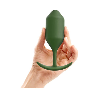Hand holding a green silicone weighted snug plug with tapered tip and curved base for comfortable wear.