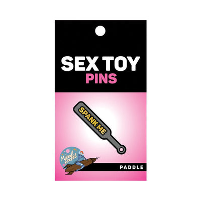 Gray enamel paddle pin with gold "Spank Me" text on pink and black Wood Rocket packaging.