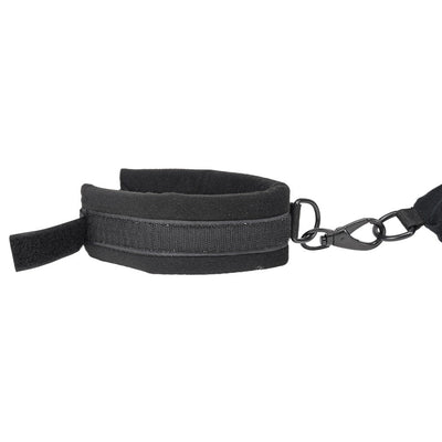 Close-up of black padded cuff with adjustable hook and loop strap and metal clasp attachment on white background.