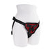 Adjustable black strap-on harness with red padded front panel displayed on white mannequin hips