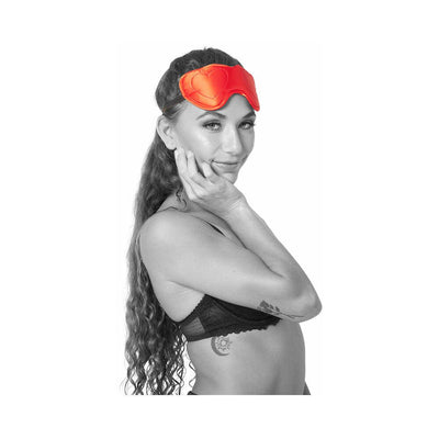 Woman wearing a red satin heart-shaped blindfold with double elastic straps and soft padding.