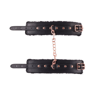 Black faux leather wrist restraints with plush lining and rose gold chain and hardware from the Sportsheets Brat bondage kit.