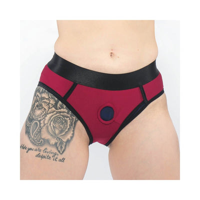 Close-up of a person wearing a red and black EmEx contour harness with a central O-ring and visible thigh tattoo.