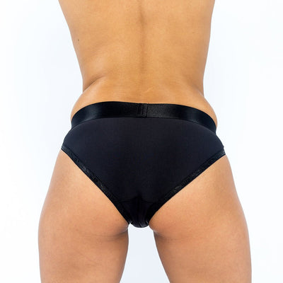 Back view of a person wearing a sleek black EmEx Silhouette harness with a smooth waistband and high-cut leg openings.