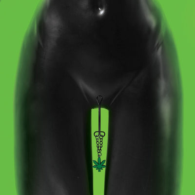 Black metal clitoral clamp with chain and green cannabis leaf charm displayed on a black mannequin against a green background.