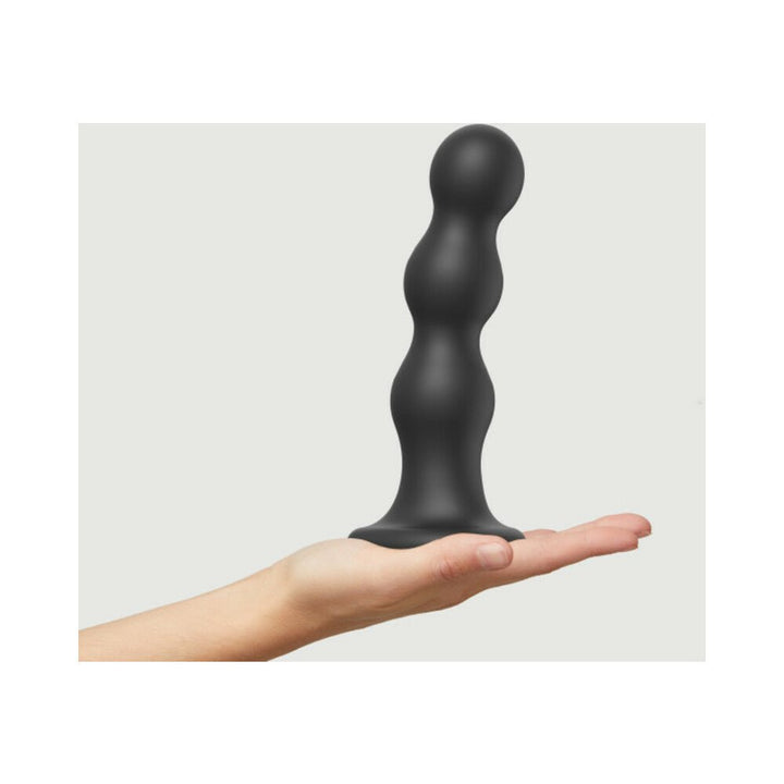 Hand holding a black silicone strap-on plug with three graduated rounded beads and a flared base.