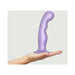Hand holding a large metallic lilac silicone dildo plug with an ergonomic curved shape and suction base.