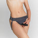 Close-up of a person wearing grey Strap-on-me harness lingerie with adjustable straps and waistband, holding a black accessory.