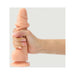 Hand holding a vanilla-colored realistic strap-on dildo with a suction base against a plain background.