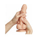 Hands holding and gently squeezing a realistic vanilla-colored silicone dildo with detailed texture and suction base.