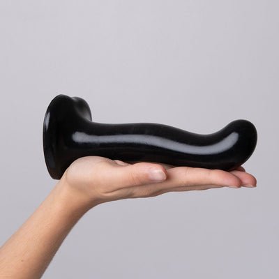 Hand holding a black silicone dildo with ergonomic curved design and suction cup base against a neutral background.