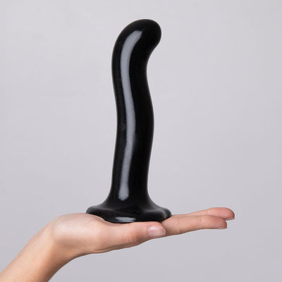 Hand holding a black silicone dildo with a curved shaft and suction cup base against a plain background.
