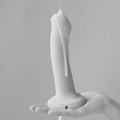 Hand holding a vanilla-colored semi-realistic silicone dildo with liquid dripping down its side.