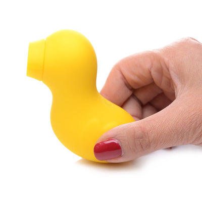 Hand holding a small yellow duck-shaped clitoral stimulator with a suction tip on a white background.